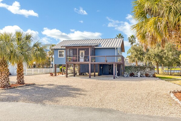 A two-story house with a balcony, surrounded by palm trees and a gravel driveway. - Coastal Getaway on canal-steps to the beach (Panacea)