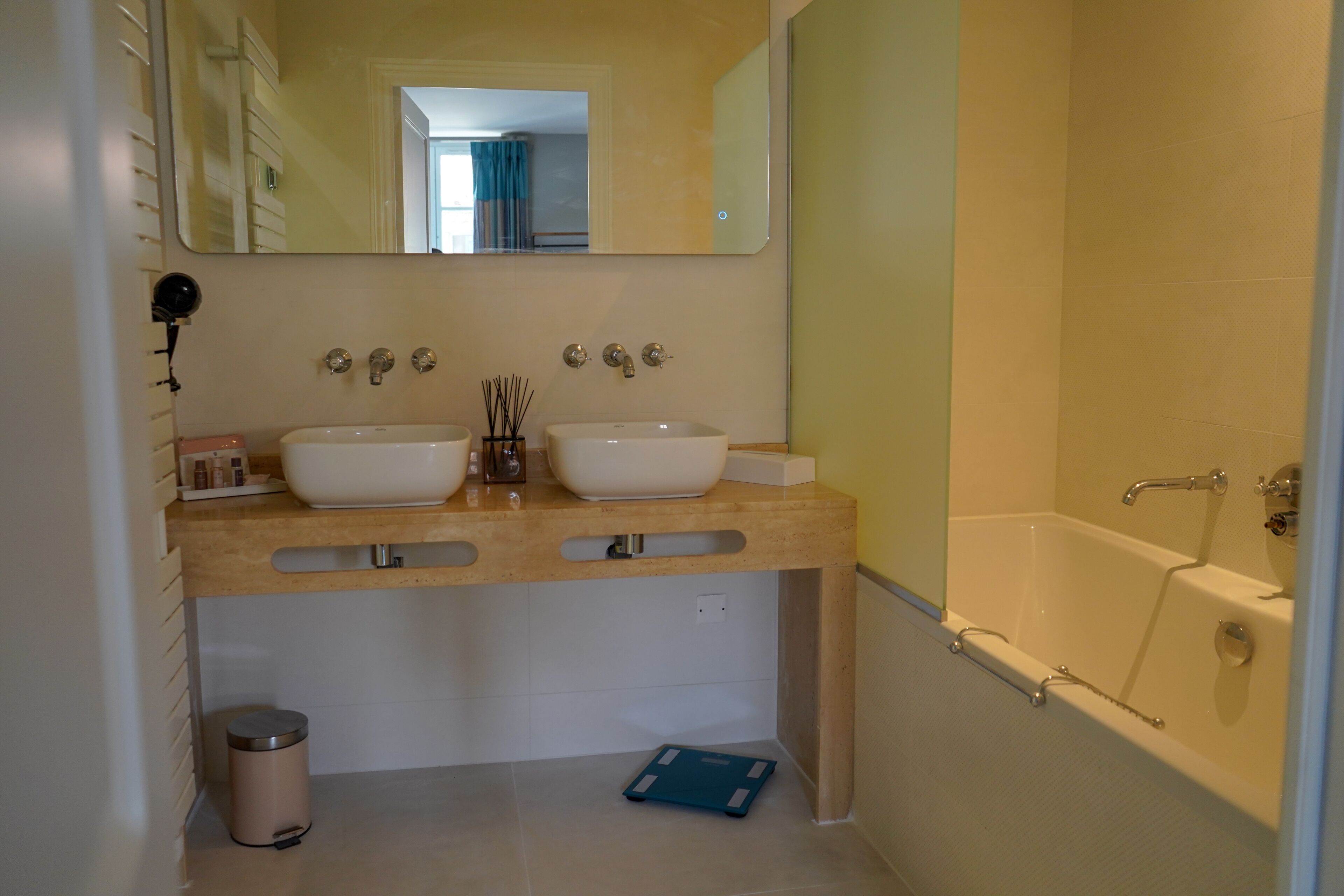 Un baño con dos lavamanos, un espejo, una bañera y un cubo de basura.
