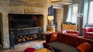 A cozy living room with a fireplace, a red sofa, a wooden coffee table, and a chandelier. - LA VILLA (Terraube)