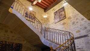 A spiral staircase with ornate metal railings, a stone wall with a framed picture, and a wooden ceiling beam. - LA VILLA (Terraube)