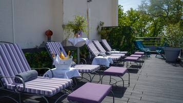 A deck with lounge chairs and tables, some with cushions, and a bucket of champagne bottles.