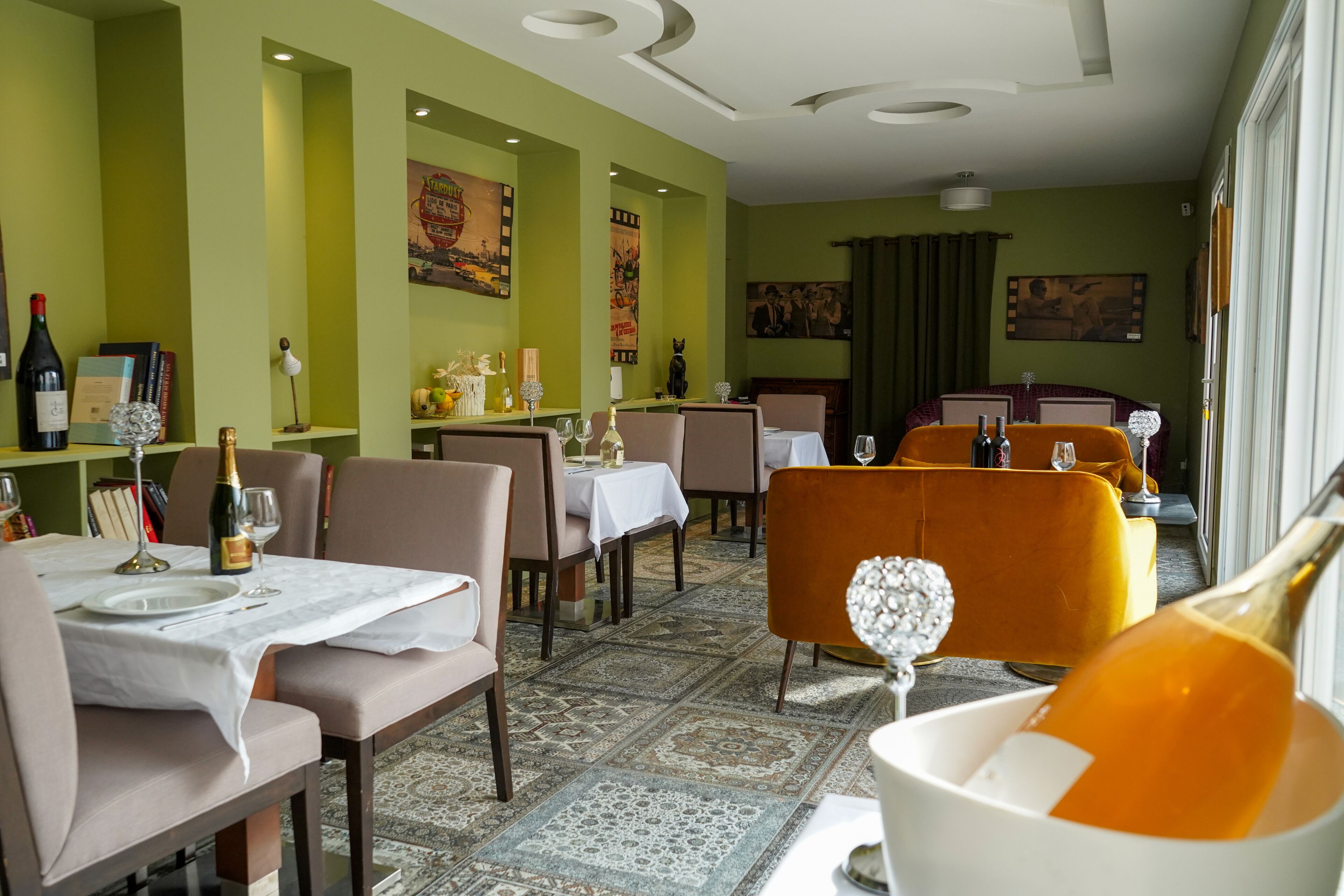 Un espace repas avec des tables préparées pour deux personnes, agrémenté d’un tapis à motifs et de murs verts.