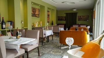 Un espace repas avec des tables préparées pour deux personnes, agrémenté d’un tapis à motifs et de murs verts.