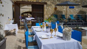 An outdoor dining area with tables set for a meal, blue chairs, and a stone building in the background. - LA VILLA (Terraube)