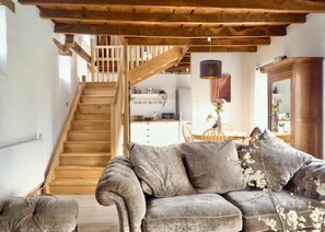 Ein gemütliches Wohnzimmer mit einer Holztreppe, einer Couch und einem Essbereich mit Tisch und Stühlen.