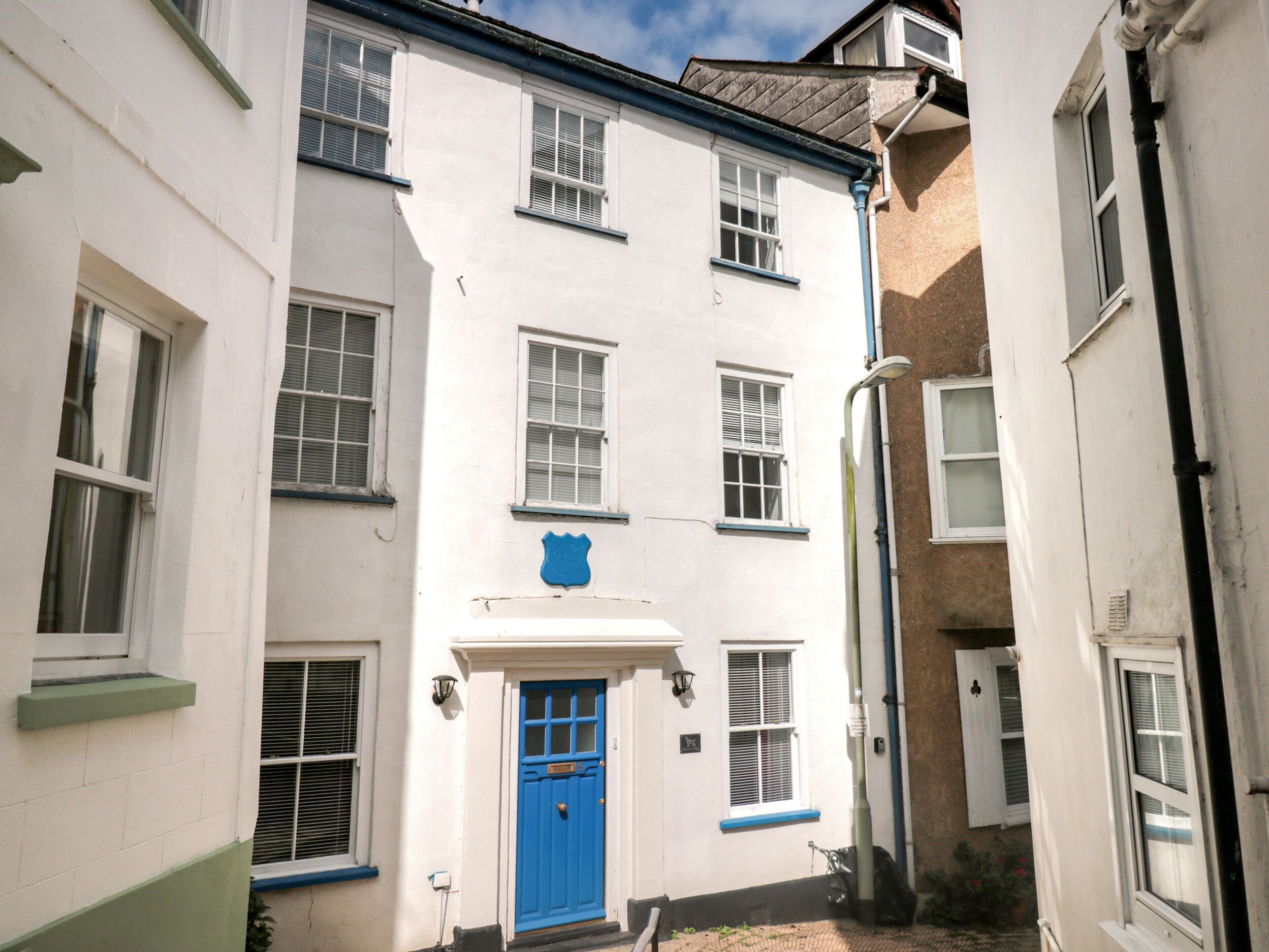 A narrow street with a white building featuring a blue door and multiple windows.
