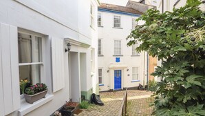 A narrow alleyway with white buildings, a blue door, and potted plants along the path.