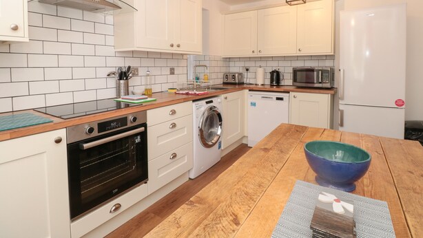 A modern kitchen with white cabinets, a wooden countertop, a built-in oven, a washing machine, a microwave, and a refrigerator.