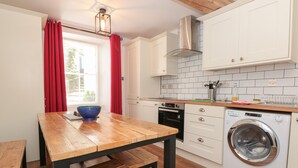 A modern kitchen with white cabinets, a built-in oven, a washing machine, and a wooden dining table with benches.