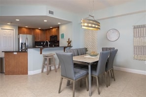 A modern kitchen with a central island, a dining table with chairs, and a pendant light.