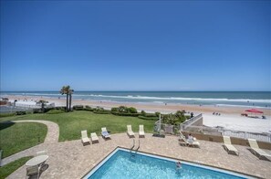 Un espace piscine avec des chaises longues, une piscine et une vue sur la plage.