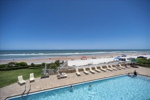 A pool area with lounge chairs and a view of the beach.