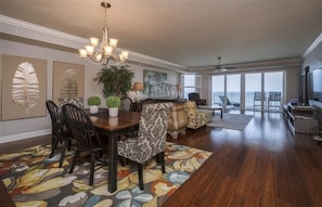 A spacious living room with a dining area, a large window offering a view, and a chandelier.