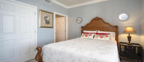 Un dormitorio con cama de madera, paredes blancas, ventilador de techo, mesita de noche con lámpara y una puerta.