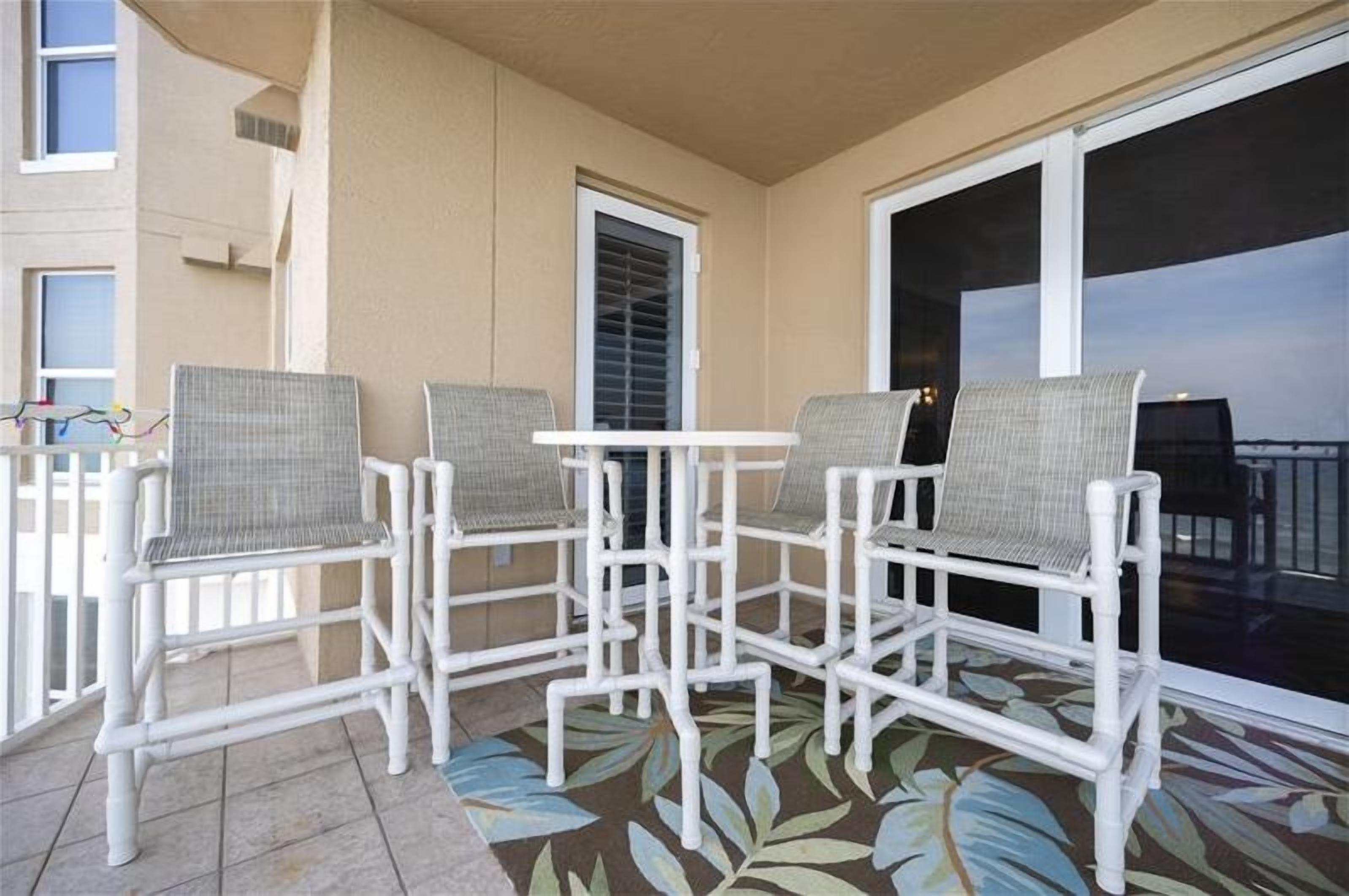 A balcony with white wicker furniture, a patterned floor, and a view of the sky.