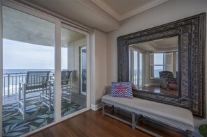Un balcón con vista al océano, un banco con un cojín estampado y un espejo grande y decorativo.