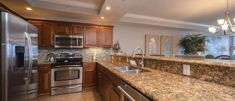 A kitchen with granite countertops, stainless steel appliances, wooden cabinets, and a built-in dishwasher.