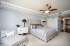 A bedroom with a bed, a nightstand, a dresser, a ceiling fan, and a door leading to another room.