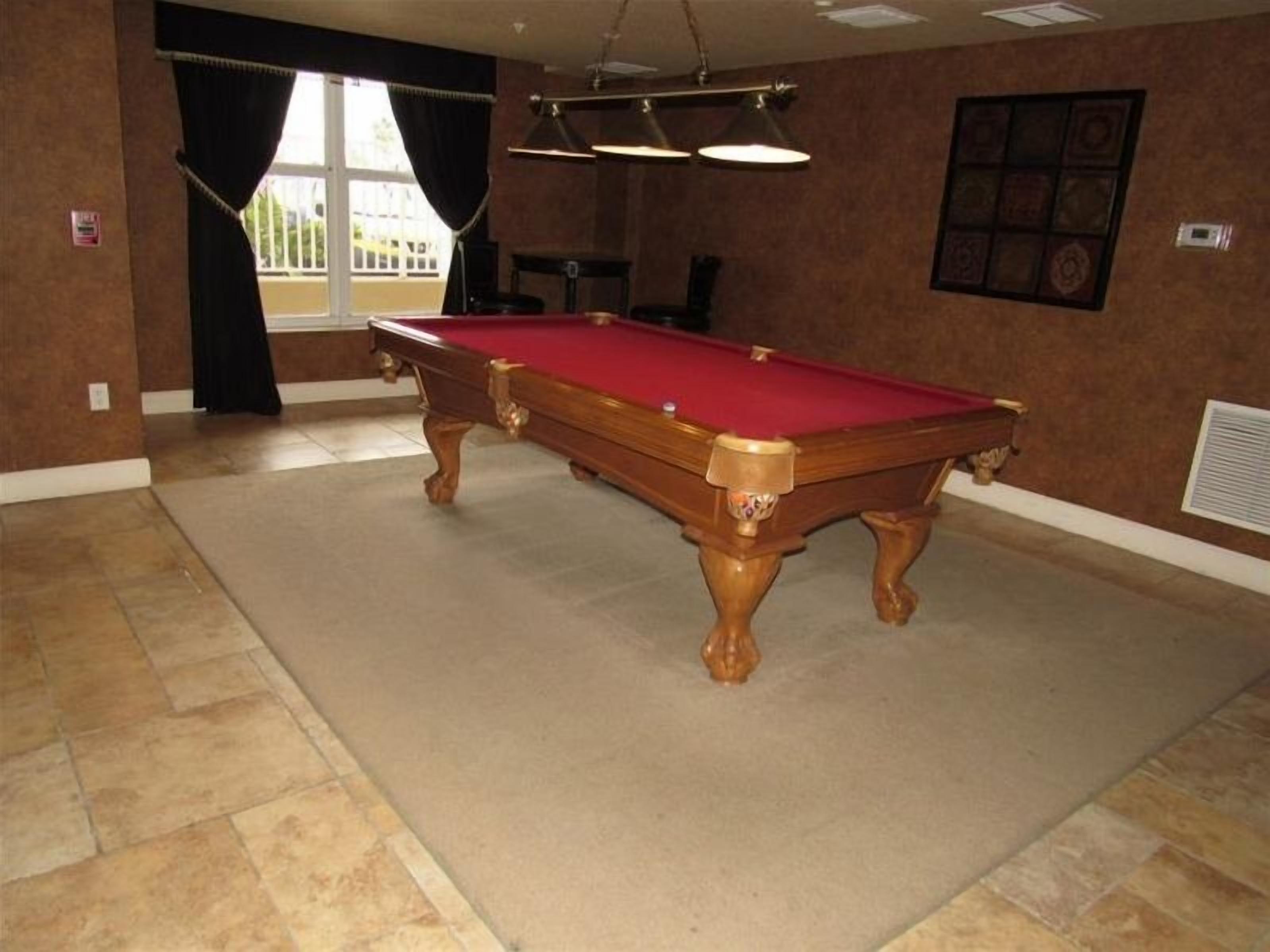 A pool table in a room with a tiled floor, a window with curtains, and a wall-mounted light fixture.