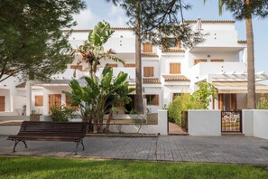 Un bâtiment blanc doté de nombreux balcons, d’une allée pavée et d’un banc.