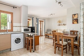 A compact kitchen with a washing machine, a microwave, and a dining area with wooden furniture.