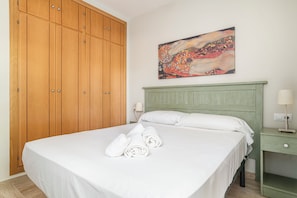 Habitación de hotel con un armario grande de madera, una cama con sábanas blancas, un cabecero verde y un cuadro en la pared.
