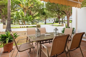 Un patio al aire libre con una mesa y sillas de vidrio, rodeado de plantas en macetas y árboles.