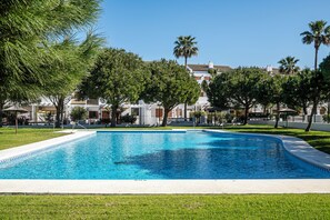 Une piscine à l’eau d’un bleu limpide, entourée d’une pelouse bien entretenue et d’arbres.