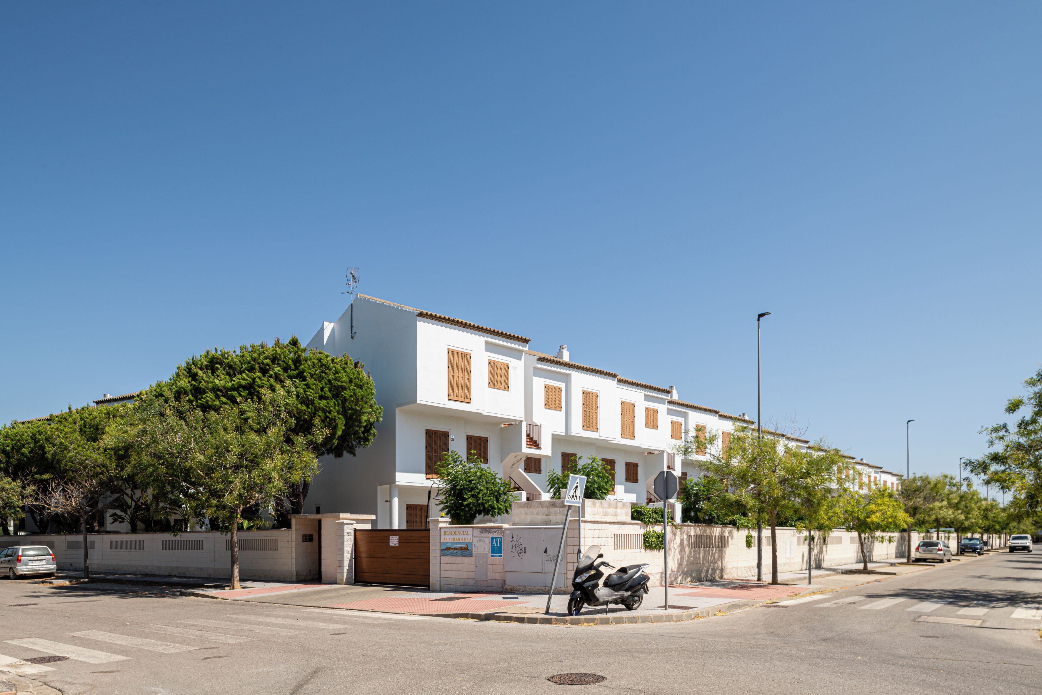 Un edificio residencial con fachada blanca, múltiples ventanas con contraventanas y un acceso con portón.