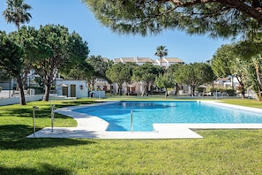 A swimming pool surrounded by grass and trees, with buildings in the background.