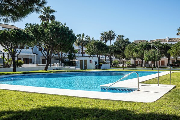 A swimming pool with a clear blue water, surrounded by grass and trees.