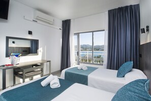 A hotel room with two beds, a desk, a large window with curtains, a view of the sea, and a mounted TV. - Hotel Base Ibiza (Sant Antoni de Portmany)