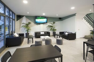 Una sala moderna con un televisor de pantalla plana, sofás, otomanas y una zona de comedor con sillas y una mesa.