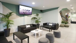 Un hall d’entrée moderne avec des canapés sombres, une table basse blanche et des poufs gris.