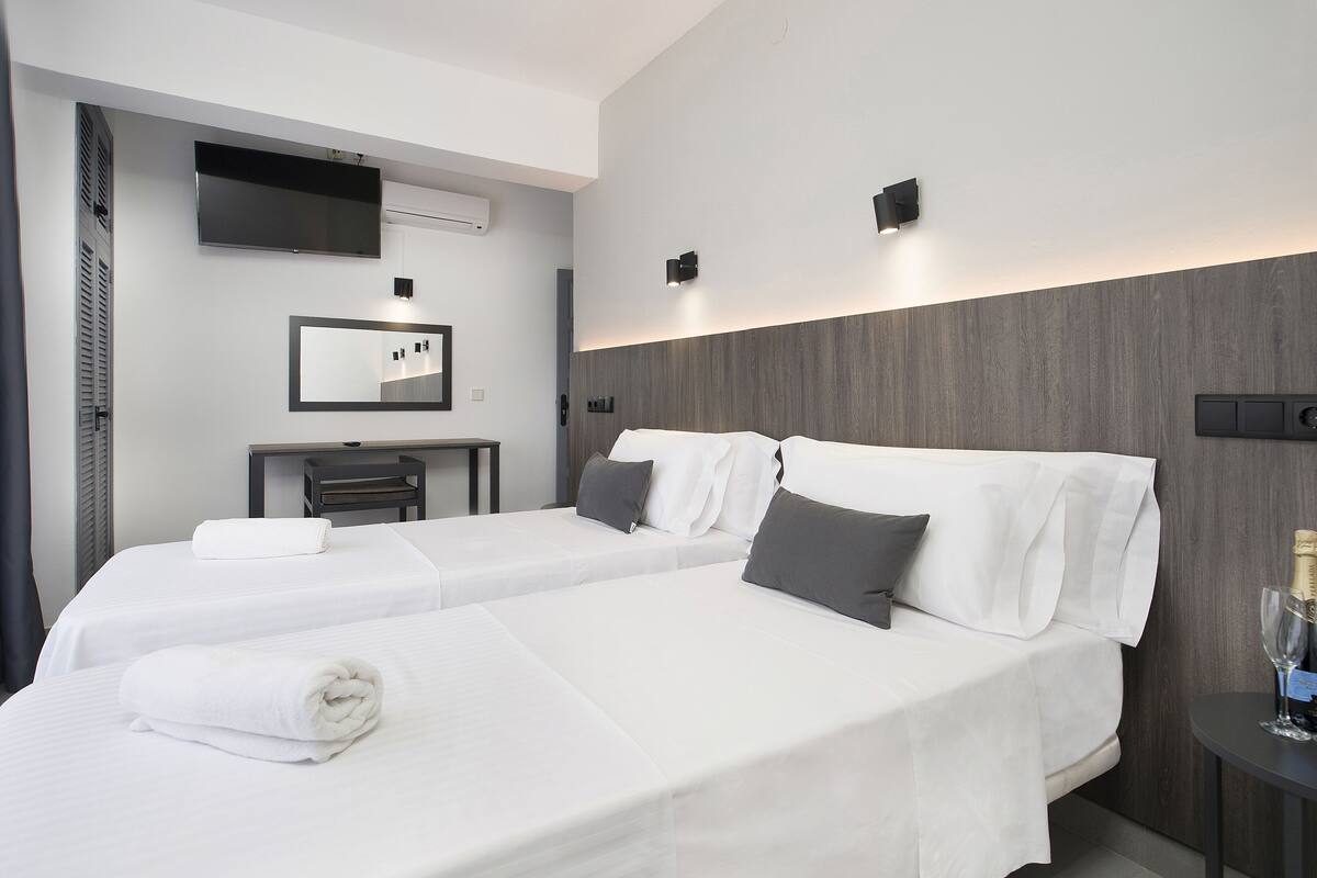 Ein Hotelzimmer mit zwei Betten, einem Schreibtisch, einem Flachbildfernseher und einer Minibar.