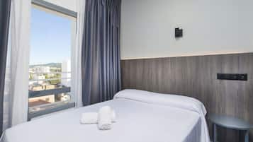 Ein Hotelzimmer mit Bett, kleinem Tisch, einem Fenster mit Vorhängen und Blick auf Gebäude.