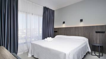 Una habitación de hotel moderna con una cama grande, una mesita de noche y vistas a través de cortinas traslúcidas.