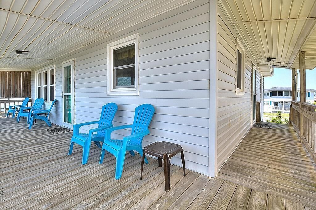 Eine überdachte Veranda mit blauen Plastikstühlen und einem kleinen hölzernen Hocker.
