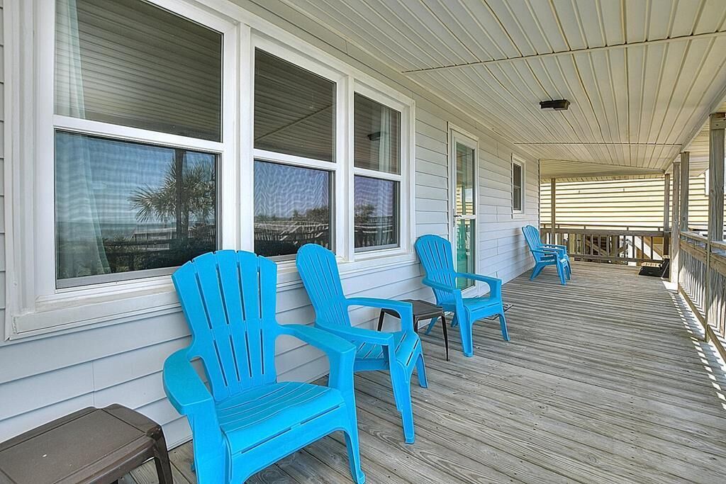 Une véranda avec des fauteuils Adirondack bleus, de grandes fenêtres et une terrasse en bois.
