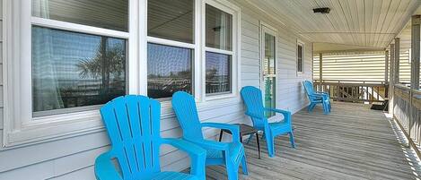 Une véranda avec des fauteuils Adirondack bleus, de grandes fenêtres et une terrasse en bois.