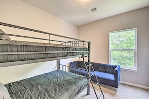 A room with bunk beds, a blue sofa, and a window with a view of greenery.