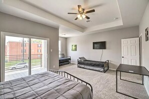 A bedroom with a bed, a desk, a ceiling fan, and a TV on the wall.