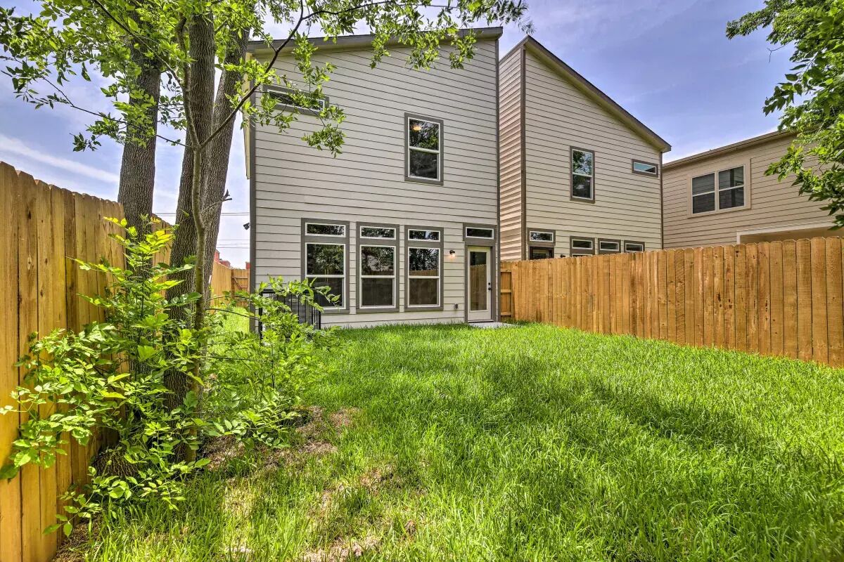 A two-story house with a fenced backyard, a wooden fence, and a small tree.