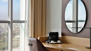A hotel room with a large window, a desk with a coffee maker, and a mirror.
