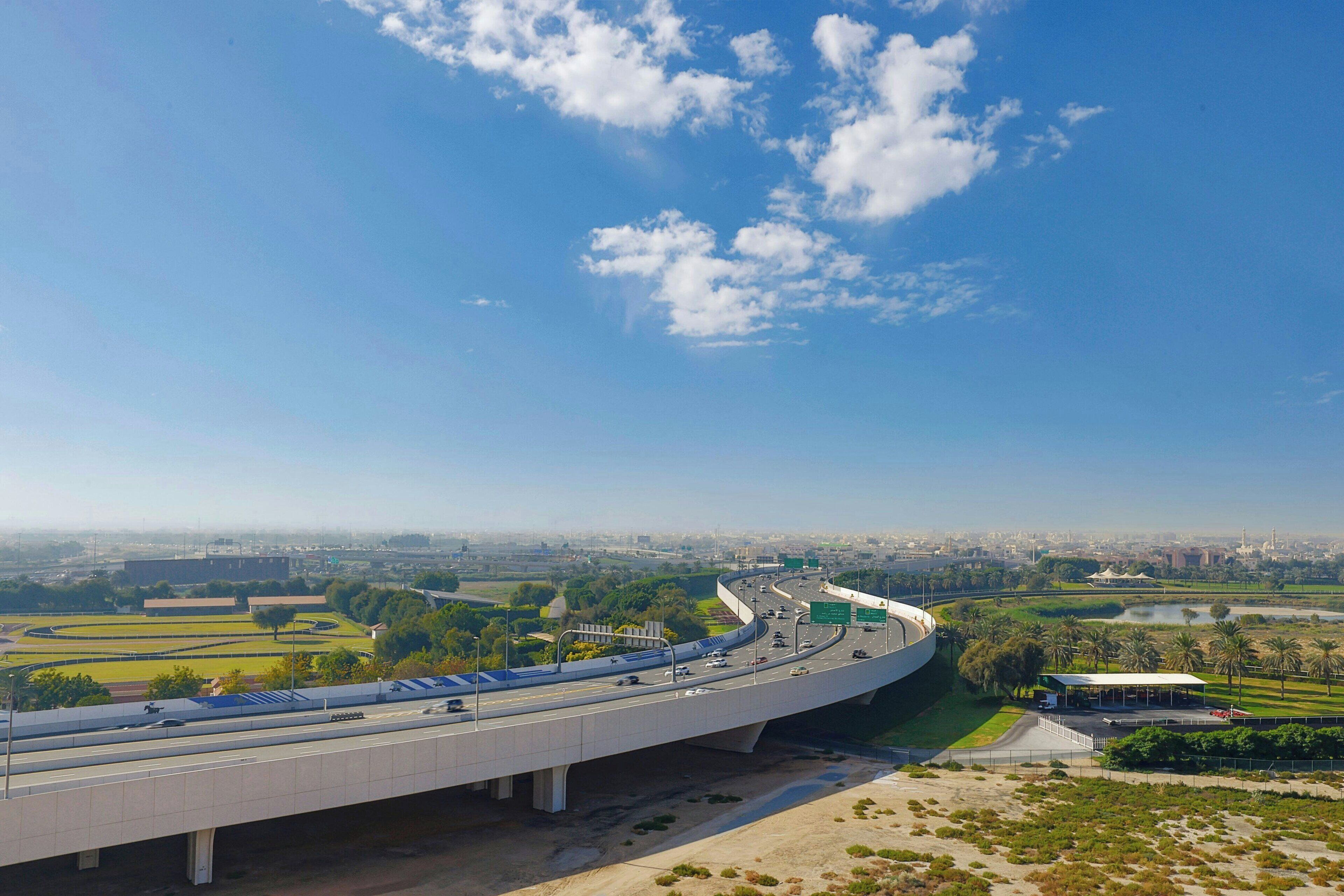 Een moderne snelweg viaduct met meerdere rijstroken, groen landschap en een heldere blauwe lucht.