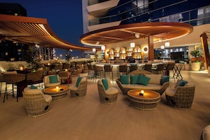 A rooftop bar with wicker furniture, a bar area, and a view of the city skyline. - The First Collection Business Bay, Dubai, a Tribute Portfolio Hotel (Dubai)