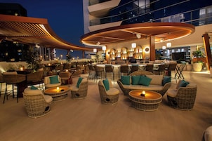 A rooftop bar with wicker furniture, a bar area, and a view of the city skyline.