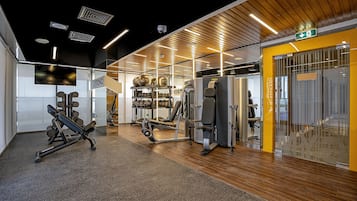 Une salle de sport équipée de matériel d’exercice, dotée d’un plancher en bois et présentant un design moderne.