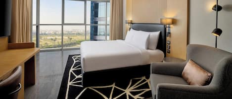 A hotel room with a large bed, a desk, a chair, a TV, and a view of the city.