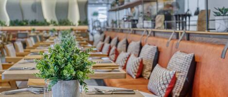 Un restaurant avec des tables en bois, des sièges rembourrés et des plantes en pot.